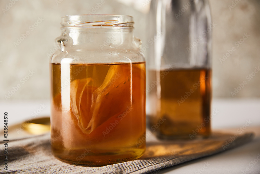 selective focus of jar with kombucha near bottle on grey napkin selective focus of jar with kombucha near bottle on grey napkin