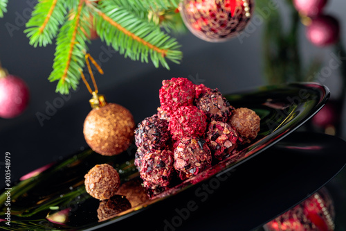 Chocolate truffles on a black plate and Christmas tree.
