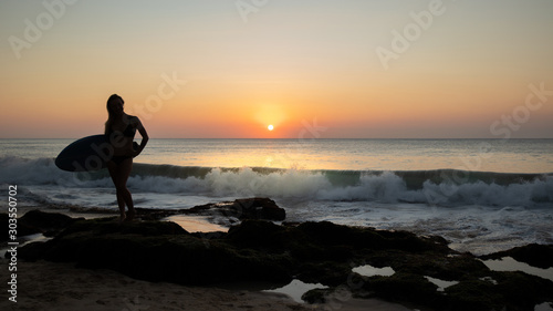Silhouette of surfer girl with surfboard at the beach. Sunset time. Tegal Wangi beach, Bali, Indonesia