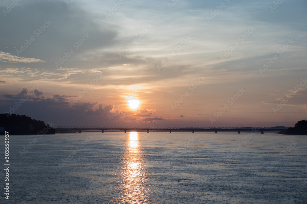 A dramatic sky with railway bridge, sunset and its shimmering reflection in tranquil water of  river Brahmaputra.