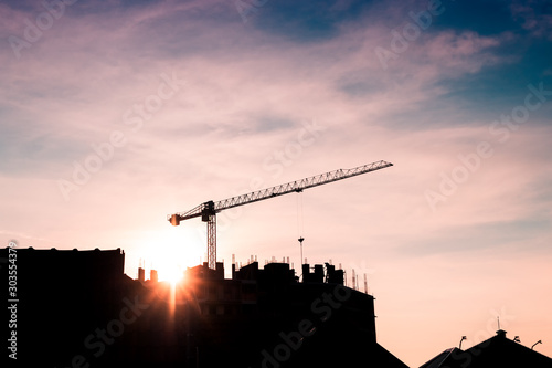Construction crane on site with silhouette of building and workers