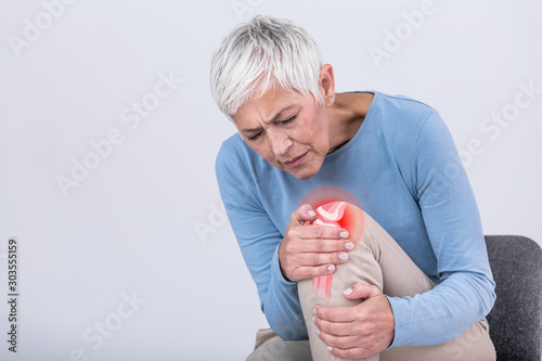 Senior woman holding the knee with pain. Old age, health problem and people concept - senior woman suffering from pain in leg at home. Elderly woman suffering from pain in knee at home photo
