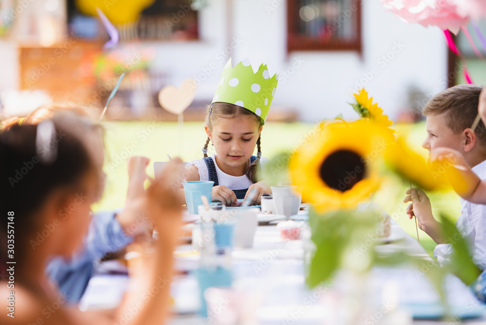 Small children sitting at the table outdoors on garden party in summer, eating. - obrazy, fototapety, plakaty 