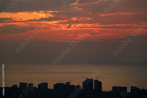Silhouette of skyscrapers and construction area with sunset sky over the sea in background 