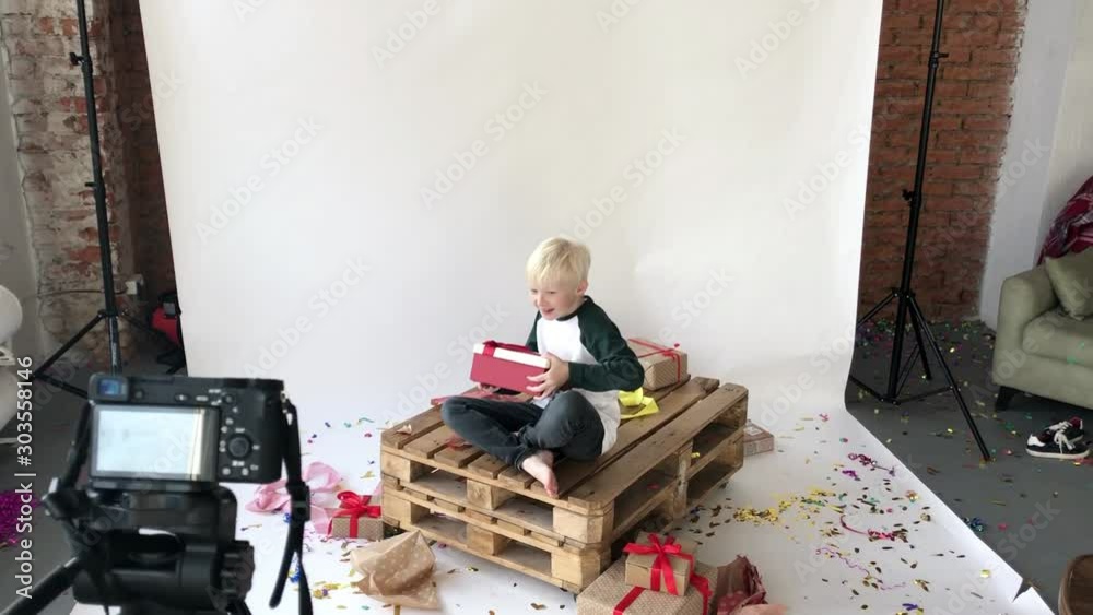 Boy blogger records the broadcast about gifts. A child sits in the studio in front of the camera with a bunch of packed gifts.