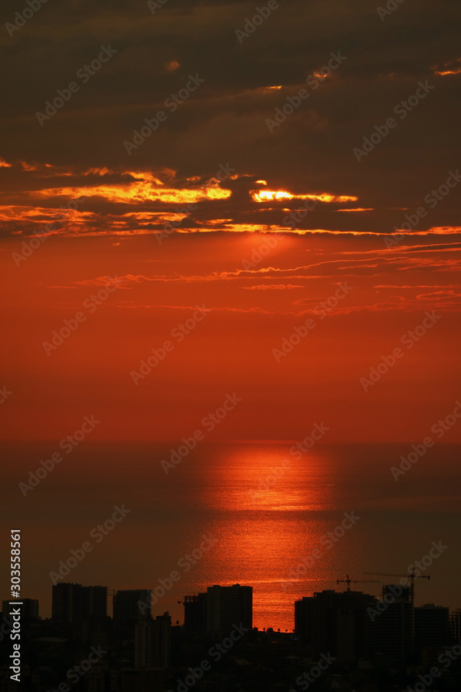 Reflections of the setting sunlight over the sea with skyscraper silhouette in foreground Reflections of the setting sunlight over the sea with skyscraper silhouette in foreground