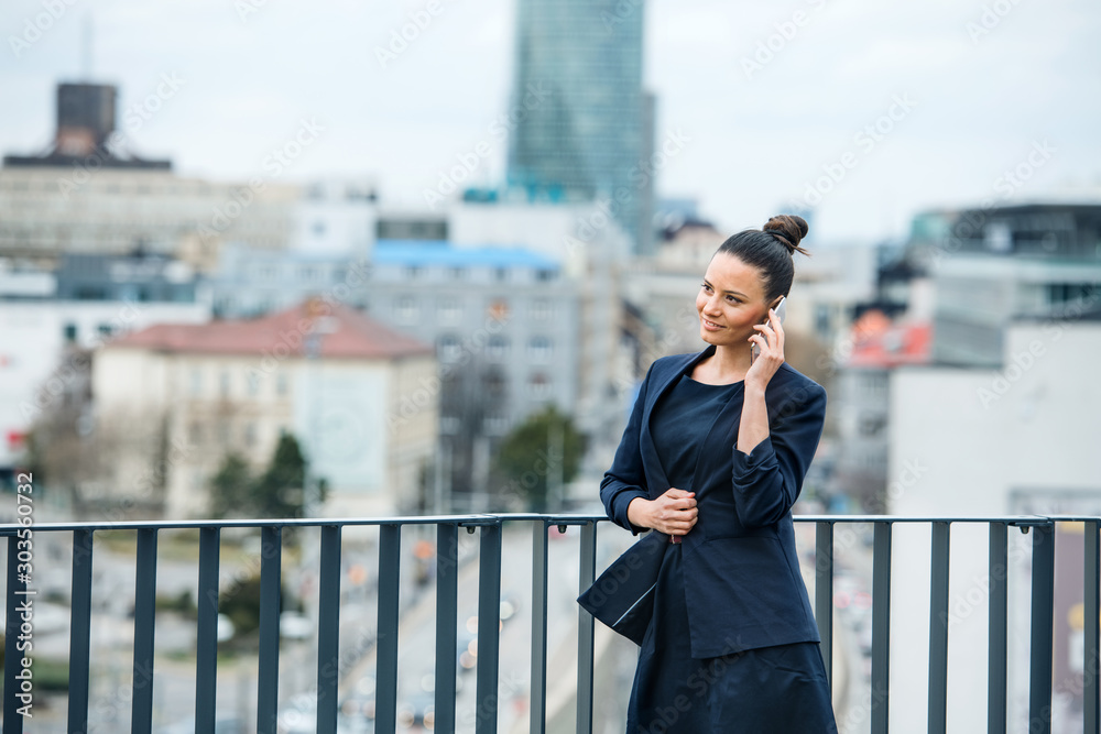 A young businesswoman standing on a terrace, making a phone call.