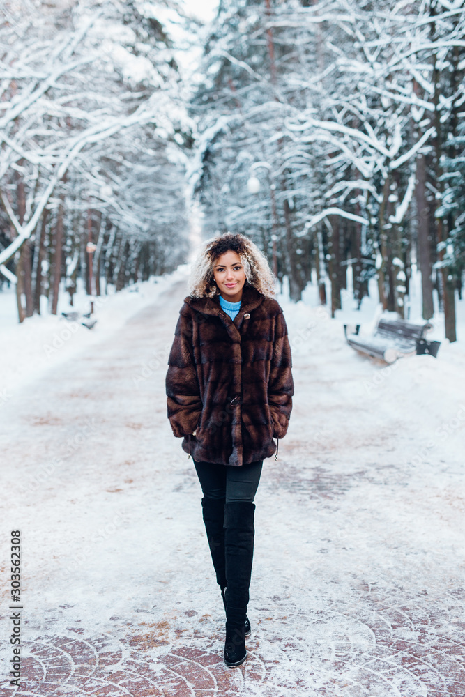 Full length portrait of afro american girl wearing in fur coat ank walking in winter park Full length portrait of afro american girl wearing in fur coat ank walking in winter park