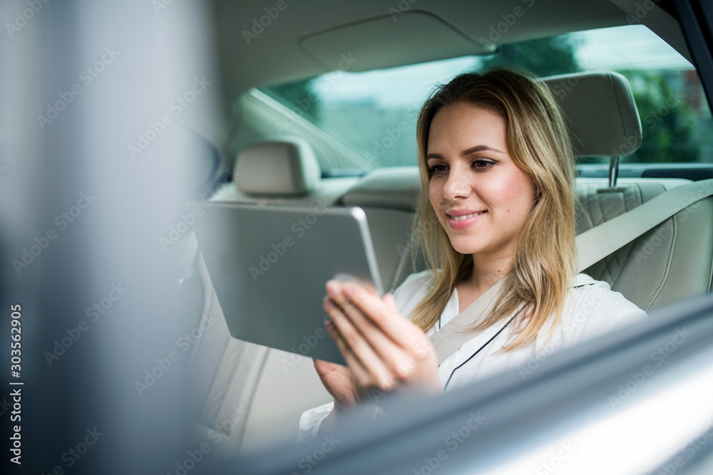 Businesswoman with tablet sitting on back seats in taxi car, working.