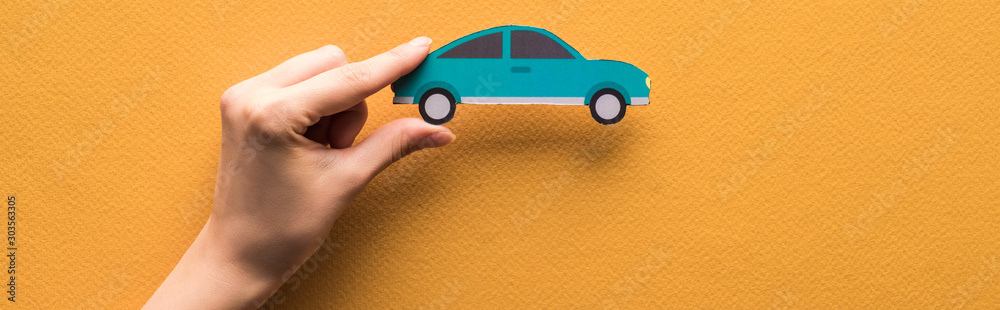 cropped view of woman holding paper cut car on orange background, panoramic shot - obrazy, fototapety, plakaty 