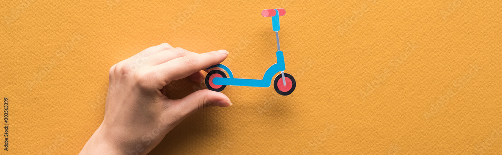 cropped view of woman holding paper cut kick scooter on orange background, panoramic shot - obrazy, fototapety, plakaty 