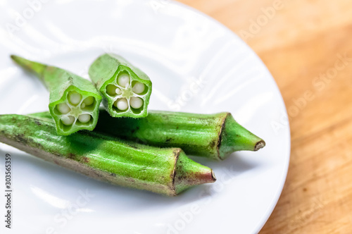 Fresh okra in white dish on wooden table.