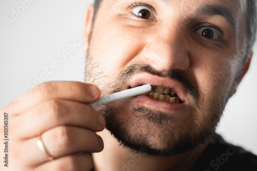 A man with bad teeth and herpes on his lip holds a cigarette near his mouth, which is much whiter than his teeth