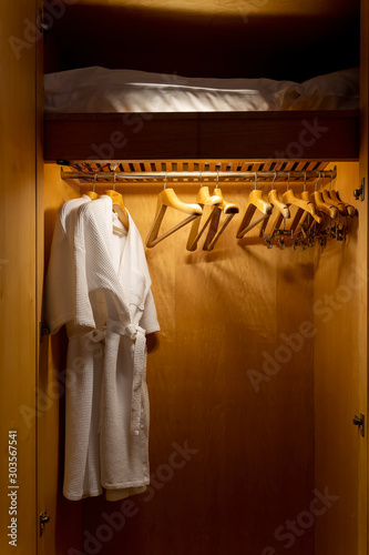 Closet white bathrobes and clothes hangers hanging on rack in the hotel wooden closet warm white low light.