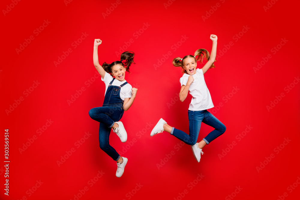 Full length photo of cheerful two small little people girlfriends celebrate triumph raise fists scream yes jump wear white t-shirt denim jeans sneakers isolated bright color background Full length photo of cheerful two small little people girlfriends celebrate triumph raise fists scream yes jump wear white t-shirt denim jeans sneakers isolated bright color background