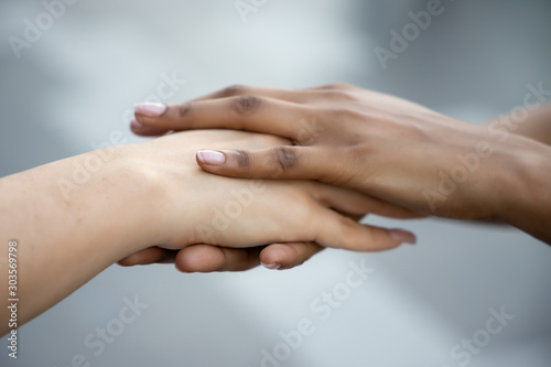 caucasian woman and african woman hand in hand, hand shaking to each other; concept of skin color tolerance, world peace, ethnicity understanding, team or teamwork