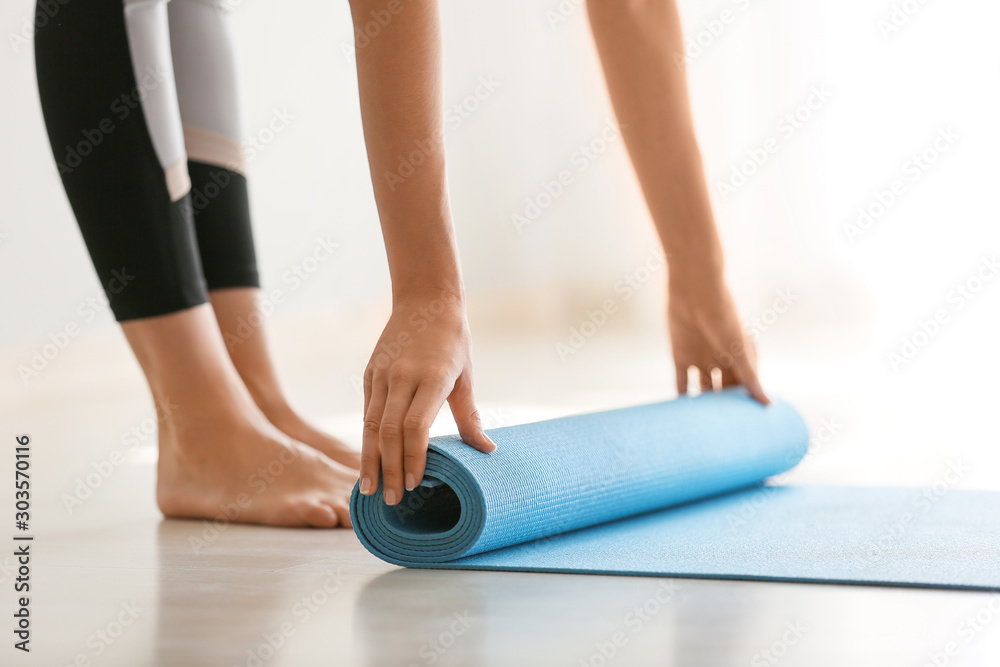 Fototapeta premium Young woman rolling yoga mat at home