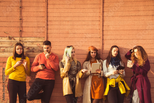 group of young people millennials using smart phones and tablets, calling, searching web, smiling, taking selfies, outdoor autumn poster ready  beautiful boy and girls