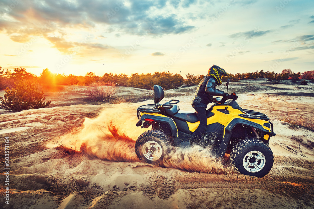 Teen riding ATV in sand dunes making a turn in the sand Teen riding ATV in sand dunes making a turn in the sand