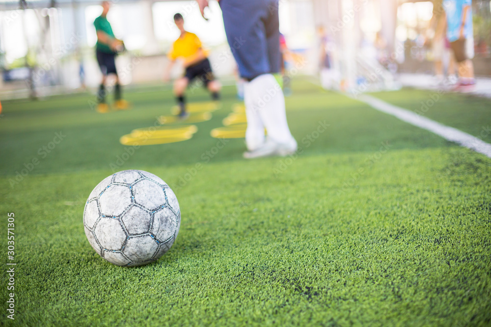 Soccer ball on green artificial turf with blurry of yellow ring marker and player training.