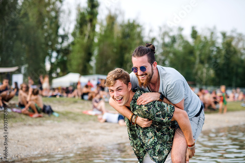 Young men friends having fun at summer festival, standing in lake.