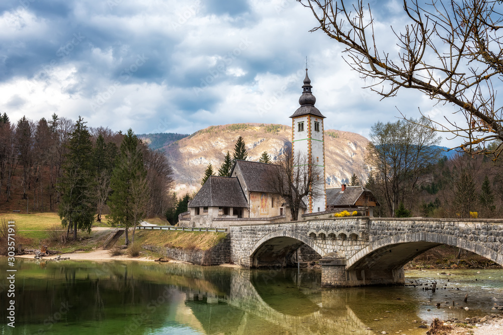 Amazing spring view of Bohinj lake with the church of St John the Baptist and the stone bridge in Triglav National Park, located in Julian Alps, Slovenia.