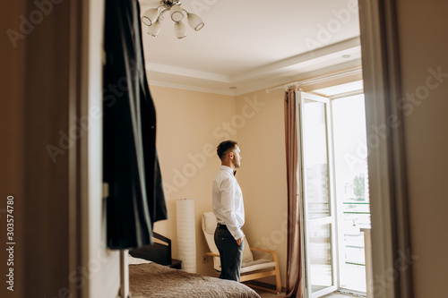 Daylight illuminates handsome groom while he stands before a window