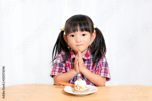 白背景でおやつのケーキを食べる前に「頂きます」をする幼い女の子。躾、マナー、行儀、幸せイメージ