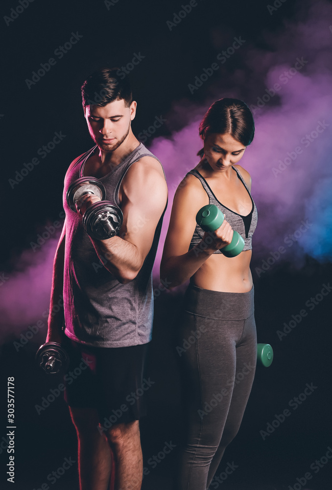 Sporty young couple with dumbbells on dark background