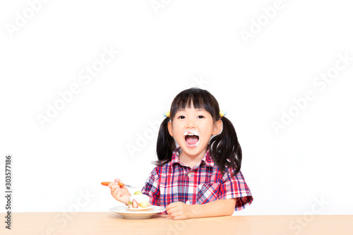 白背景でおやつのケーキを楽しそうに食べる幼い女の子。幸せ、成長、健康イメージ
