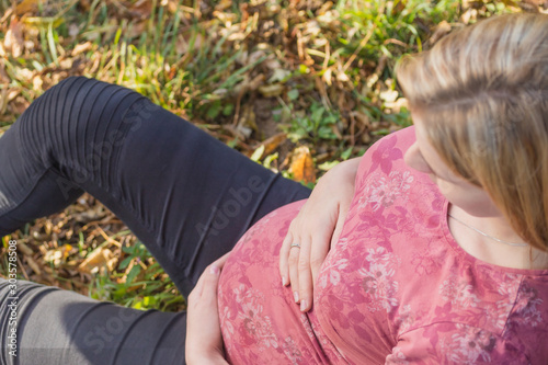 Top view of young pregnant woman sitting and holding her belly. Horizontally. 