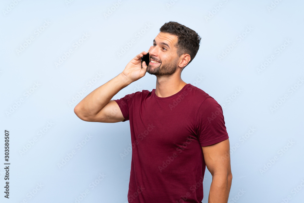 Handsome man over isolated blue background keeping a conversation with the mobile phone Handsome man over isolated blue background keeping a conversation with the mobile phone