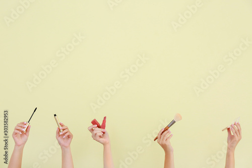 Many hands with decorative cosmetics and brush on color background