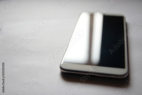 A smartphone with a protective film on the screen reflects sunlight. The modern business phone lies against a grey background.