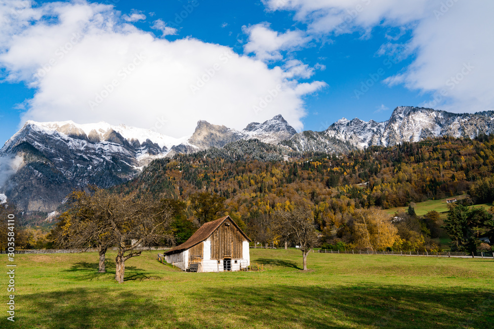 mountain landscape with fall color forest and snow-capped mountain peaks and barn in foreground