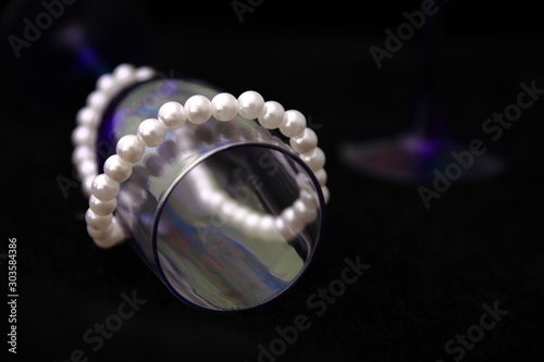 Fuger lying on a black soft lint surface surrounded by pearl decoration. The glare on a glass of blue glass.