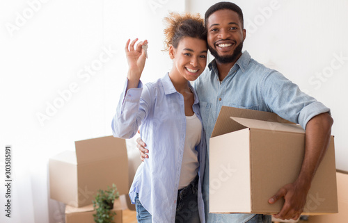 Couple Showing Key Holding Moving Box Standing In New Home