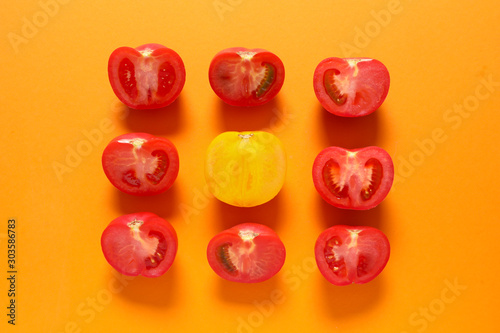 Foto Yellow tomato among red ones on color background