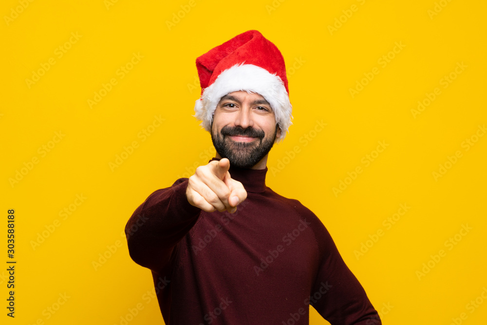 Man with christmas hat over isolated yellow background points finger at you with a confident expression Man with christmas hat over isolated yellow background points finger at you with a confident expression