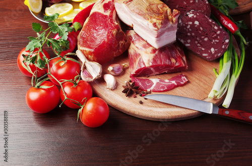 Meat products, balyk and sausages surrounded by vegetables and greens on the table