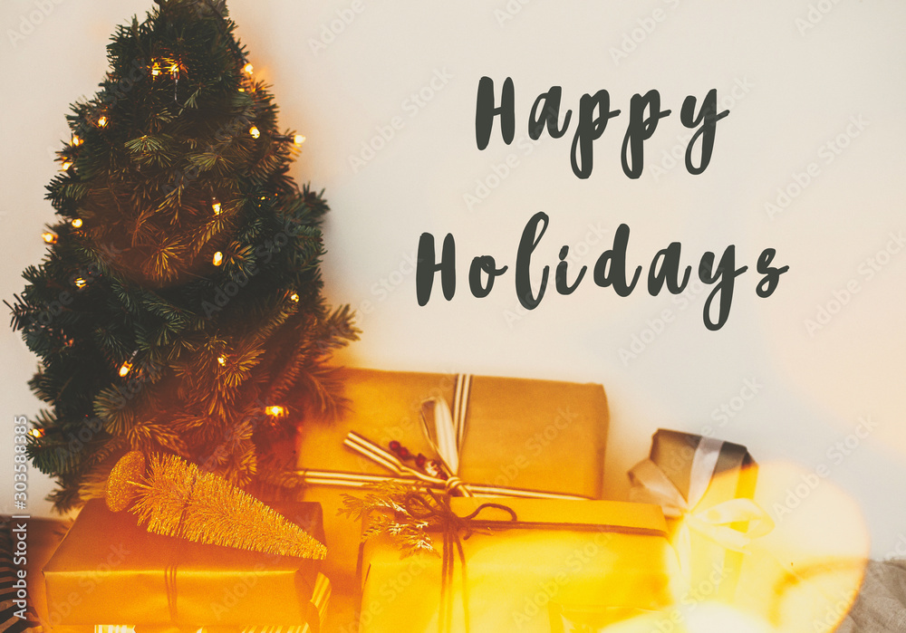 Φωτογραφία Happy Holidays text sign on christmas tree in golden lights bokeh with festive stylish gifts in white room