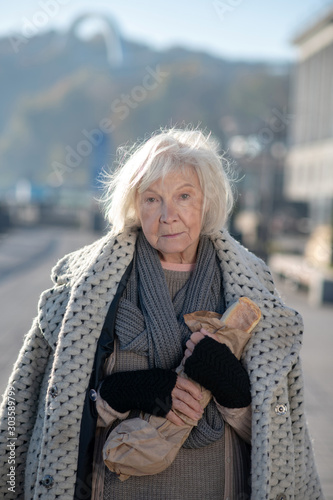 Poor homeless woman wearing warm coat holding bread photo