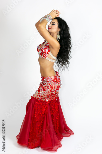 Brunette in a beautiful long red dress to perform belly dance a white background.