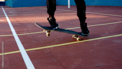 male skateboarder skating in action in a skatepark with long black pants and sneakers with sports field background and buildings © Fernando