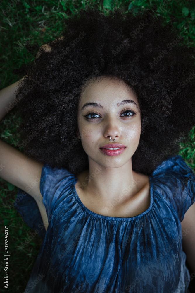 Φωτογραφία Portrait of a young black woman lying on the grass in a park at sunset - Millenn
