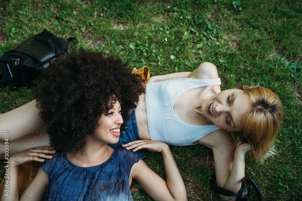 Φωτογραφία Couple of young women is lying on the grass in a meadow on a summer day at the p