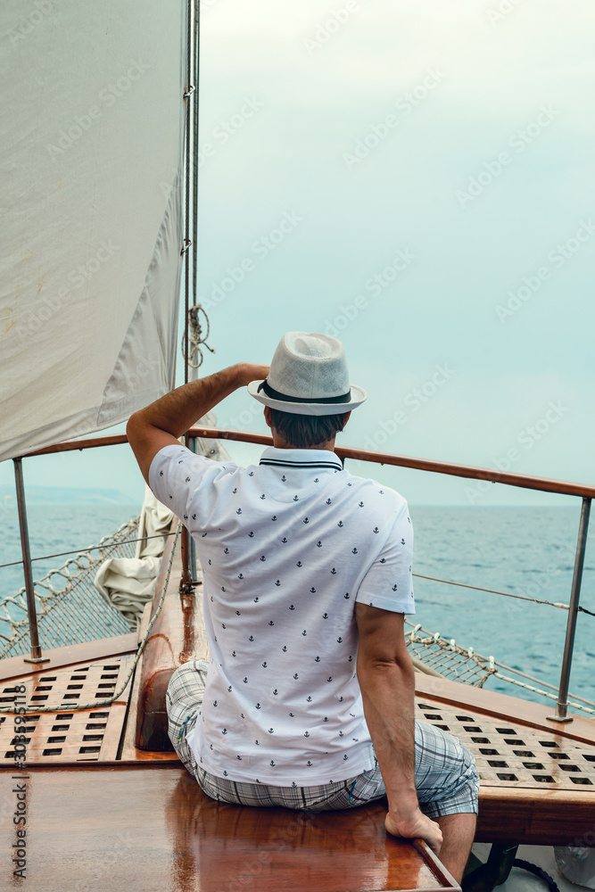 Stylish, young man on deck of a cruise ship, looking into the distance against the blue sky. Concept of sea travel and recreation