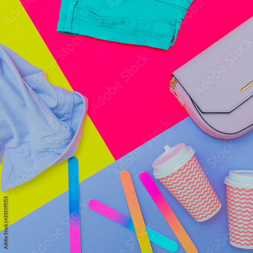 Fashionable laid out set: blue denim jacket, pink handbag, turquoise jeans and coffee cups on bright colorful background. flat lay, above view, mockup