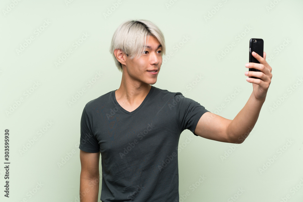 Young asian man over isolated green background making a selfie Young asian man over isolated green background making a selfie