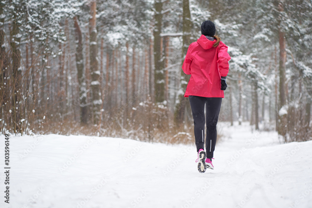Woman wearing pink sport outfit runing in winter forest, view from back, copy space